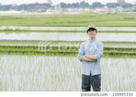 一位年輕的農民站在稻田間的小路上。 一位年輕的農民站在稻田間的小路上。 139995330