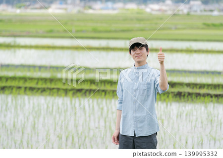 A young farmer stands on the path between rice paddies. A young farmer stands on the path between rice paddies. 139995332
