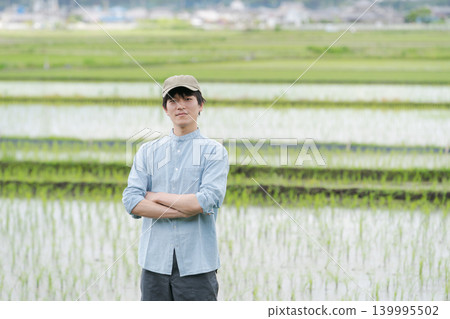 A young farmer stands on the path between rice paddies. 139995502