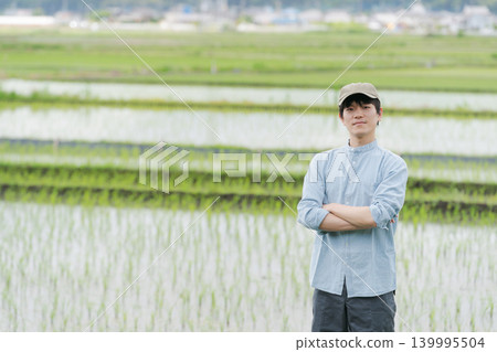 A young farmer stands on the path between rice paddies. A young farmer stands on the path between rice paddies. 139995504