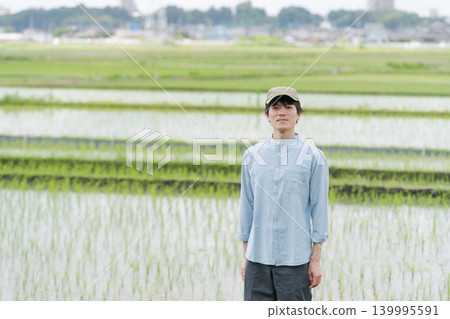 A young farmer stands on the path between rice paddies. 139995591