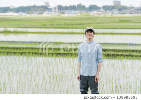 A young farmer stands on the path between rice paddies. 139995593