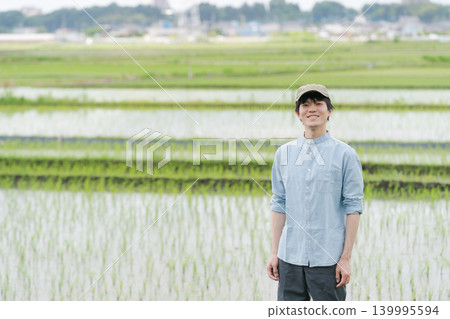 A young farmer stands on the path between rice paddies. 139995594