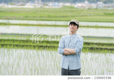 一位年輕的農民站在稻田間的小路上。 139995596