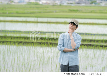 一位年輕的農民站在稻田間的小路上。 一位年輕的農民站在稻田間的小路上。 139996313