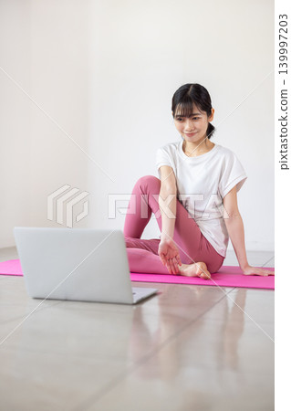 A young Japanese woman practices yoga while looking at her laptop. A young Japanese woman practices yoga while looking at her laptop. 139997203