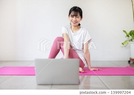 一位年輕的日本女性一邊看著筆記型電腦一邊練習瑜珈。 139997204