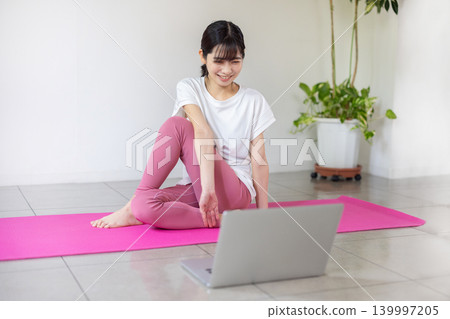 一位年輕的日本女性一邊看著筆記型電腦一邊練習瑜珈。 139997205