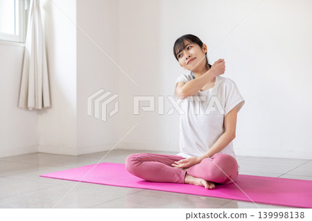 一位年輕的日本女子在瑜珈墊上為自己做肩部按摩。 139998138