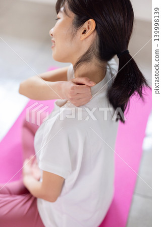 一位年輕的日本女子在瑜珈墊上為自己做肩部按摩。 139998139