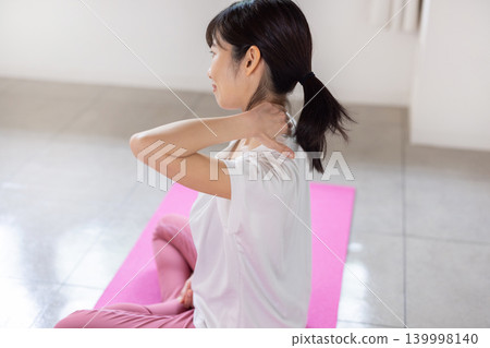 一位年輕的日本女子在瑜珈墊上為自己做肩部按摩。 139998140