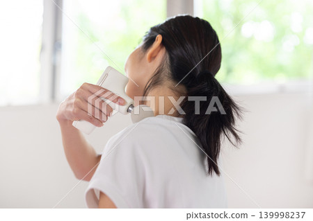 一位年輕的日本女性在瑜珈墊上用按摩槍按摩肩膀。 139998237