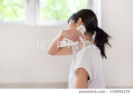 一位年輕的日本女性在瑜珈墊上用按摩槍按摩肩膀。 139998239