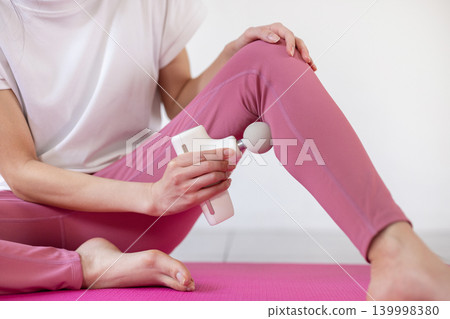 特寫鏡頭拍攝一位女士在瑜珈墊上用按摩槍按摩雙腳。 139998380