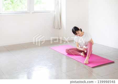 一位年輕的日本女子在瑜珈墊上用按摩槍為自己按摩腿部。 139998548