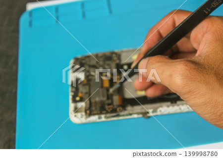 Technician Repairing Smartphone Motherboard with Precision Tweezers, Mobile Phone Repair Close Up Technician Repairing Smartphone Motherboard with Precision Tweezers, Mobile Phone Repair Close Up 139998780