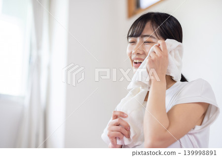 一位年輕的日本女子麵帶微笑，用毛巾擦了擦額頭的汗。 139998891