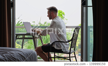 Man Typing On Laptop At Hotel Balcony Workspace During Remote Work Routine, Digital Nomad Lifestyle And Flexible Online Business Concept Man Typing On Laptop At Hotel Balcony Workspace During Remote Work Routine, Digital Nomad Lifestyle And Flexible Online Business Concept 139999150