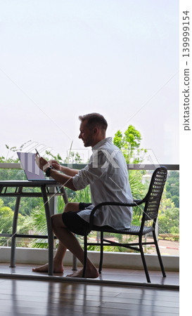 Man Using Smartphone Near Laptop At Hotel Balcony Workspace During Remote Work Routine, Digital Nomad Lifestyle And Mobile Productivity Concept Man Using Smartphone Near Laptop At Hotel Balcony Workspace During Remote Work Routine, Digital Nomad Lifestyle And Mobile Productivity Concept 139999154