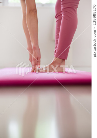特寫鏡頭拍攝一位女性在瑜珈墊上做前屈伸展動作時，她的指尖和腳。 139999170