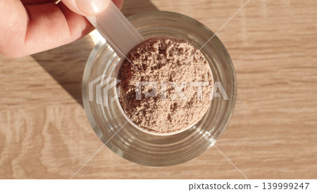 Top View Chocolate Whey Protein Scoop Above Glass Cup, Sports Nutrition And Homemade Protein Shake Preparation Top View Chocolate Whey Protein Scoop Above Glass Cup, Sports Nutrition And Homemade Protein Shake Preparation 139999247