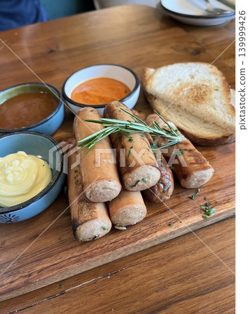A platter of grilled sausages and toast served on a wooden plate with sauce. A platter of grilled sausages and toast served on a wooden plate with sauce. 139999426