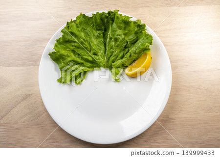 一份清爽的沙拉,由新鮮生菜和檸檬組成,盛放在白色盤子裡。 一份清爽的沙拉,由新鮮生菜和檸檬組成,盛放在白色盤子裡。 139999433
