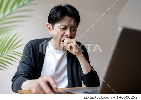 A middle-aged man working while fighting off sleepiness 140000252