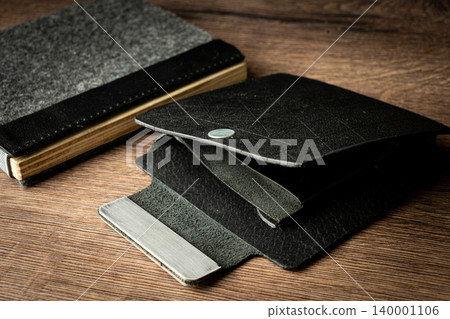Handmade black wallet made of genuine leather on a wooden background. Close-up, top view. Handmade black wallet made of genuine leather on a wooden background. Close-up, top view. 140001106