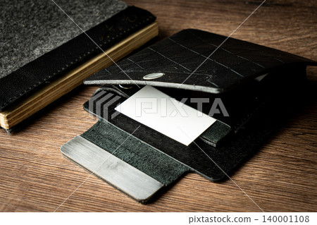 Handmade black wallet made of genuine leather on a wooden background. Close-up, top view. Handmade black wallet made of genuine leather on a wooden background. Close-up, top view. 140001108