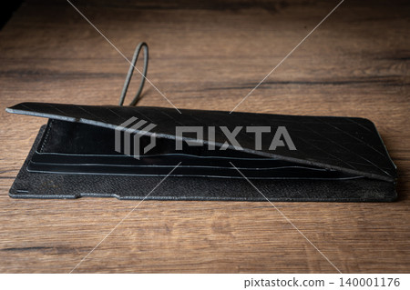 Handmade black wallet made of genuine leather on a wooden background. Close-up, top view. Handmade black wallet made of genuine leather on a wooden background. Close-up, top view. 140001176