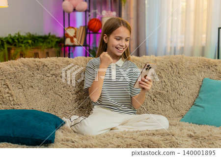 Child girl kid playing mobile game app on smartphone at home, smiling and celebrating happy victory 140001895