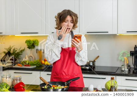 Young woman upset after bad smartphone message during home cooking feeling loss failure and defeat 140001909