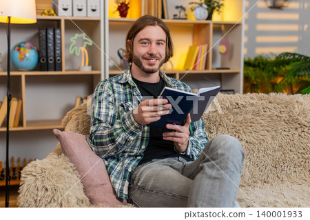 Young man on home sofa writing task list in notebook and planning daily routine in calm living room Young man on home sofa writing task list in notebook and planning daily routine in calm living room 140001933