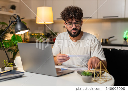 Arabian man balances accounts with laptop and calculator enters sums marks paid checks late night up Arabian man balances accounts with laptop and calculator enters sums marks paid checks late night up 140002008