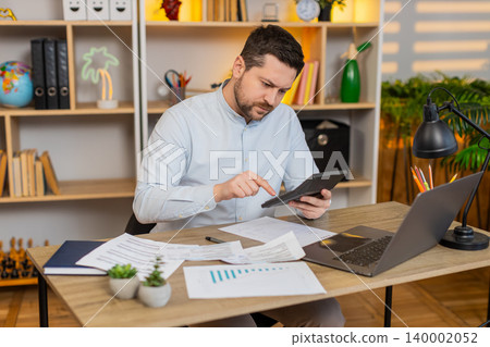 Young man on home table checking bills and reacting to unexpected payments with frustration stress Young man on home table checking bills and reacting to unexpected payments with frustration stress 140002052