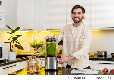 Middle-aged man blending banana smoothie in home kitchen listening to music on headphones for diet Middle-aged man blending banana smoothie in home kitchen listening to music on headphones for diet 140002064
