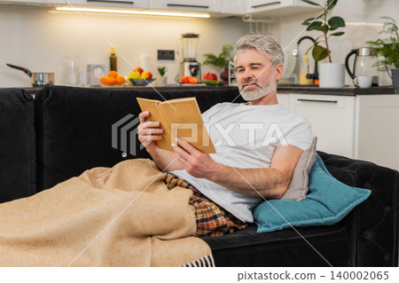 Middle-aged man reads book under plaid smiles enjoys free time comfort relax leisure chill rest 140002065