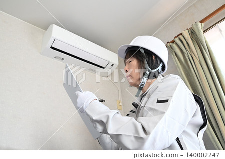 Image of a female worker inspecting an air conditioner. 140002247
