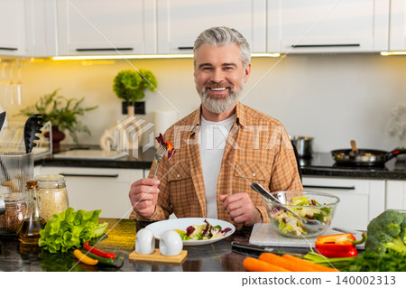 Middle-aged man serving fresh vegetable salad on plate in home kitchen smiling for healthy diet meal Middle-aged man serving fresh vegetable salad on plate in home kitchen smiling for healthy diet meal 140002313