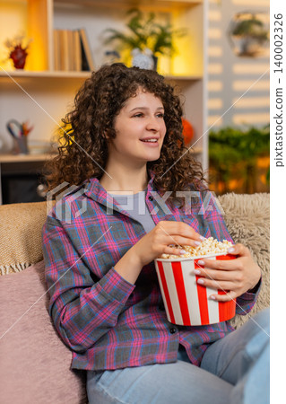 Young woman on home sofa watching fun film with popcorn laughing in surprise during home movie night Young woman on home sofa watching fun film with popcorn laughing in surprise during home movie night 140002326