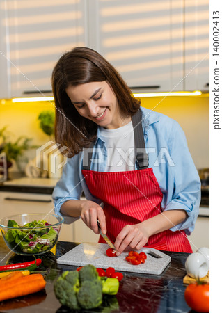 Young woman making fresh vegetable salad in home kitchen for healthy diet weight loss nutrition plan 140002413