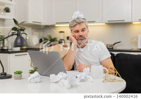 Middle-aged man drafts project notes at table burnout fatigue low motivation crumpled paper at home Middle-aged man drafts project notes at table burnout fatigue low motivation crumpled paper at home 140002416