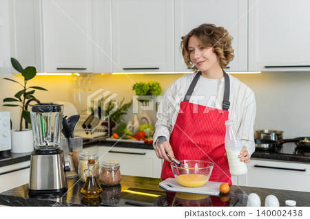 Young woman whisking eggs with milk for healthy breakfast meal prep and cooking in cozy home kitchen Young woman whisking eggs with milk for healthy breakfast meal prep and cooking in cozy home kitchen 140002438