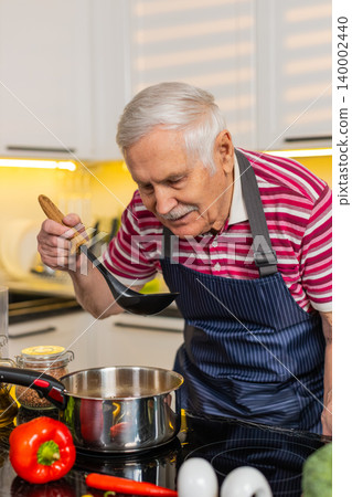 Senior old man tasting fresh soup in home kitchen smiling while cooking healthy diet dinner recipe Senior old man tasting fresh soup in home kitchen smiling while cooking healthy diet dinner recipe 140002440