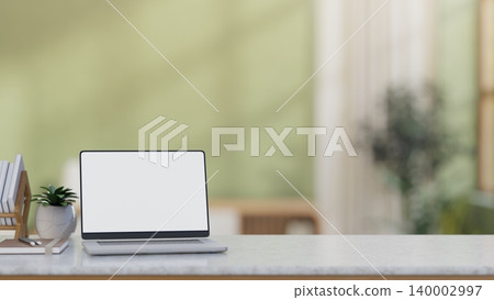 White screen laptop beside bookrack and potted plant on marble countertop table in a green wall room White screen laptop beside bookrack and potted plant on marble countertop table in a green wall room 140002997