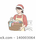 A woman wearing an apron and headscarf holds a laundry basket full of clothes, ready to do the washing in front of a washing machine. 140003064