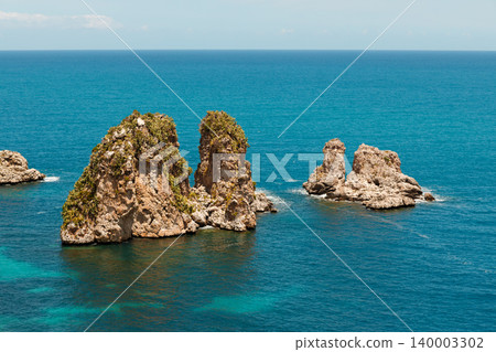 Jagged rock formations covered in green vegetation emerge from the clear blue ocean, evoking a sense of tropical paradise and summer adventure Jagged rock formations covered in green vegetation emerge from the clear blue ocean, evoking a sense of tropical paradise and summer adventure 140003302
