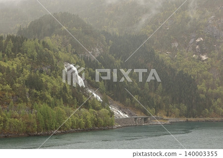 Furebergsfossen Waterfall. A view of Furebergsfossen a glacier fed waterfall. The waterfall flows under the road and directly into the Maurangerfjord, an arm of the Hardangerfjord in Norway. Furebergsfossen Waterfall. A view of Furebergsfossen a glacier fed waterfall. The waterfall flows under the road and directly into the Maurangerfjord, an arm of the Hardangerfjord in Norway. 140003355