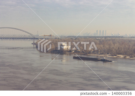 Bridge and barge on the river with city on background. Spring Kyiv landmark with Dnipro river, Ukraine. Water transport concept. Transportation bridge over the water. Big city in dawn dusk. Bridge and barge on the river with city on background. Spring Kyiv landmark with Dnipro river, Ukraine. Water transport concept. Transportation bridge over the water. Big city in dawn dusk. 140003356